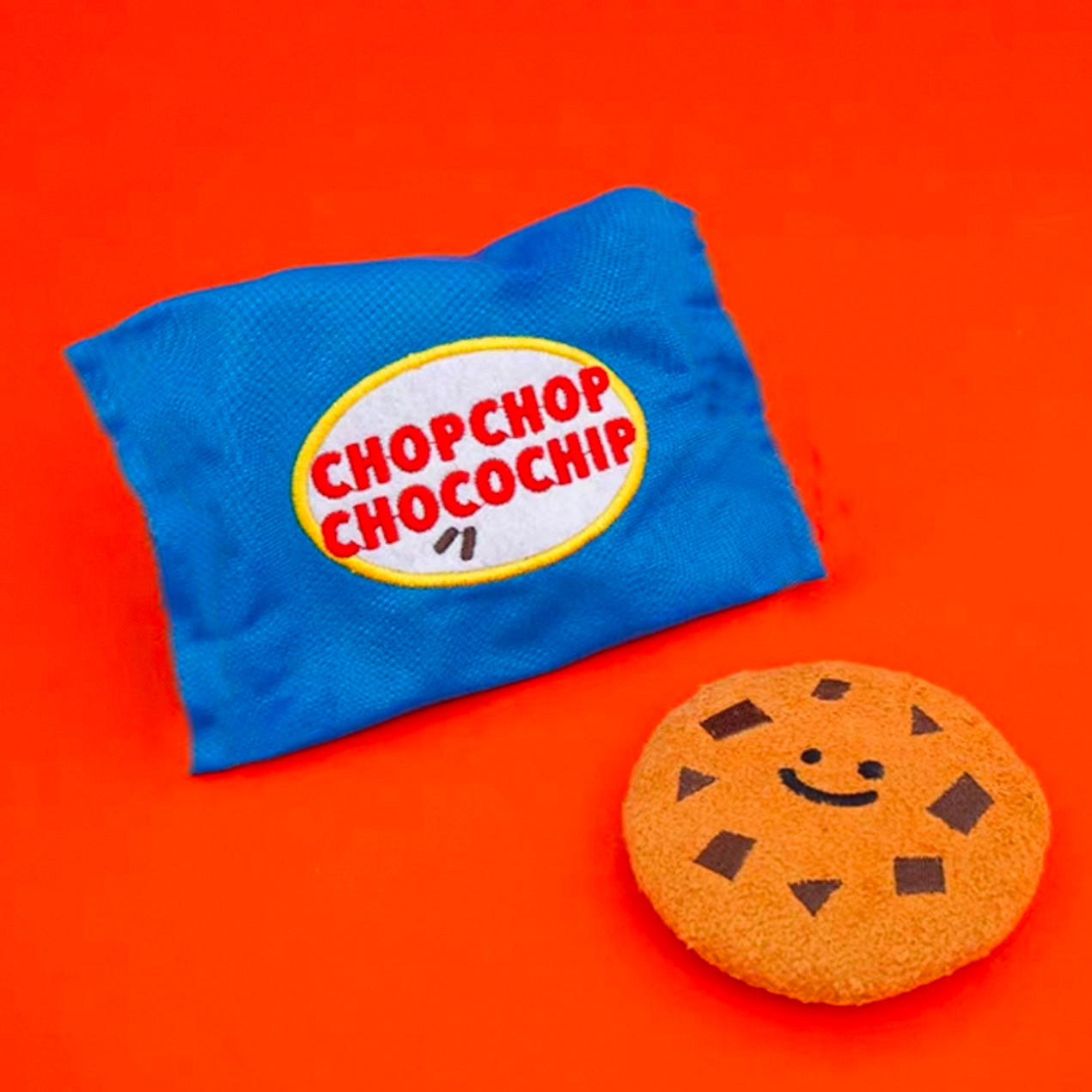 A blue crinkle dog toy designed to look like a chocolate chip cookie, with the text 'CHOPCHOP CHOCOCHIP' on the packaging.