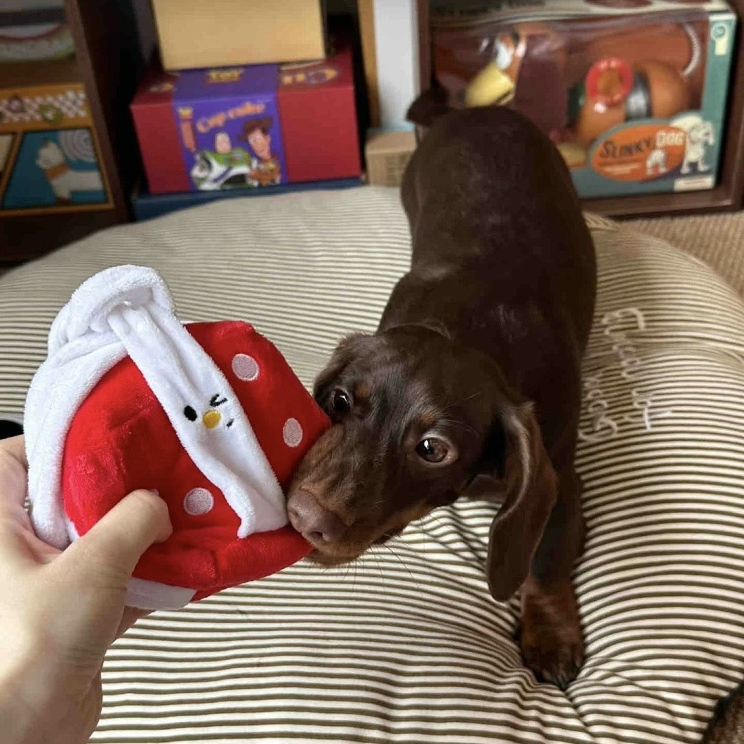 Dog playing with a red and white plush toy on a striped cushion