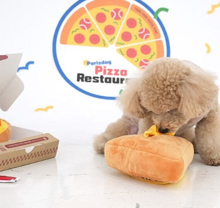 Dog playing with a plush toy shaped like a pizza slice in front of a Parisdog Pizza Restaurant sign.