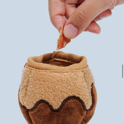 Hand holding a piece of food over a small, brown, fabric cup with a textured surface on a light blue background.